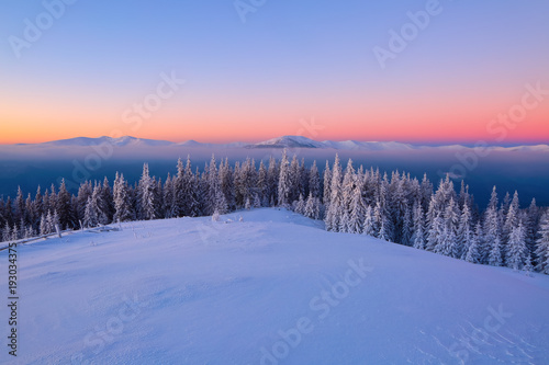 Fantastic scenery with the high mountains in snow, dense textured fog and a sunrise in the cold winter day.