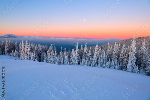 Fantastic scenery with the high mountains in snow, dense textured fog and a sunrise in the cold winter day.