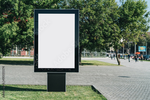 Vertical blank glowing billboard on the city street. In the background buildings and road with cars. Mock up. The poster on the street next to the roadway. photo