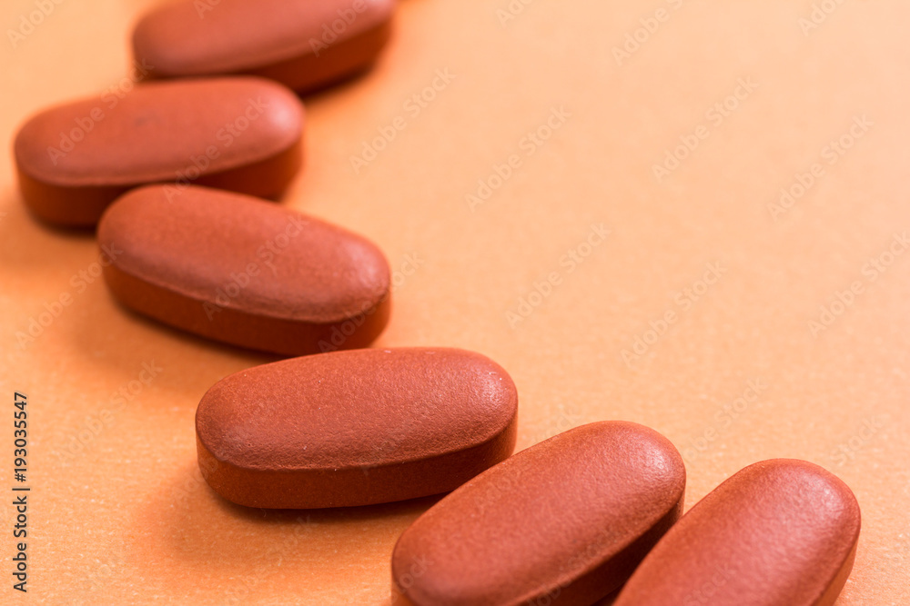 Heap of brown capsules on orange table.