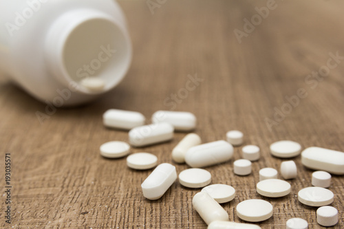 Heap of white capsules on wooden table.