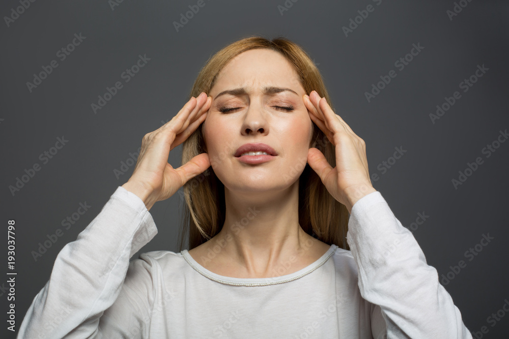 Stressful day. Portrait of unhappy blonde woman standing with eyes closed and holding her hands on temples expressing pain. Isolated on background Stressful day. Portrait of unhappy blonde woman standing with eyes closed and holding her hands on temples expressing pain. Isolated on background
