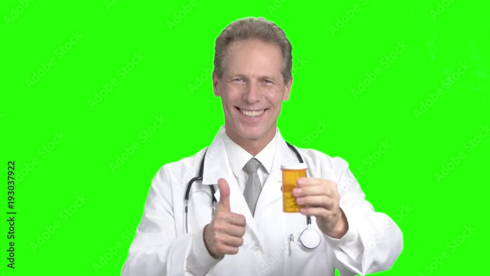 Smiling doctor on chroma key background. Middle aged cheerful doctor holding container with medicine and gesturing ok, green background. Smiling doctor on chroma key background. Middle aged cheerful doctor holding container with medicine and gesturing ok, green background.