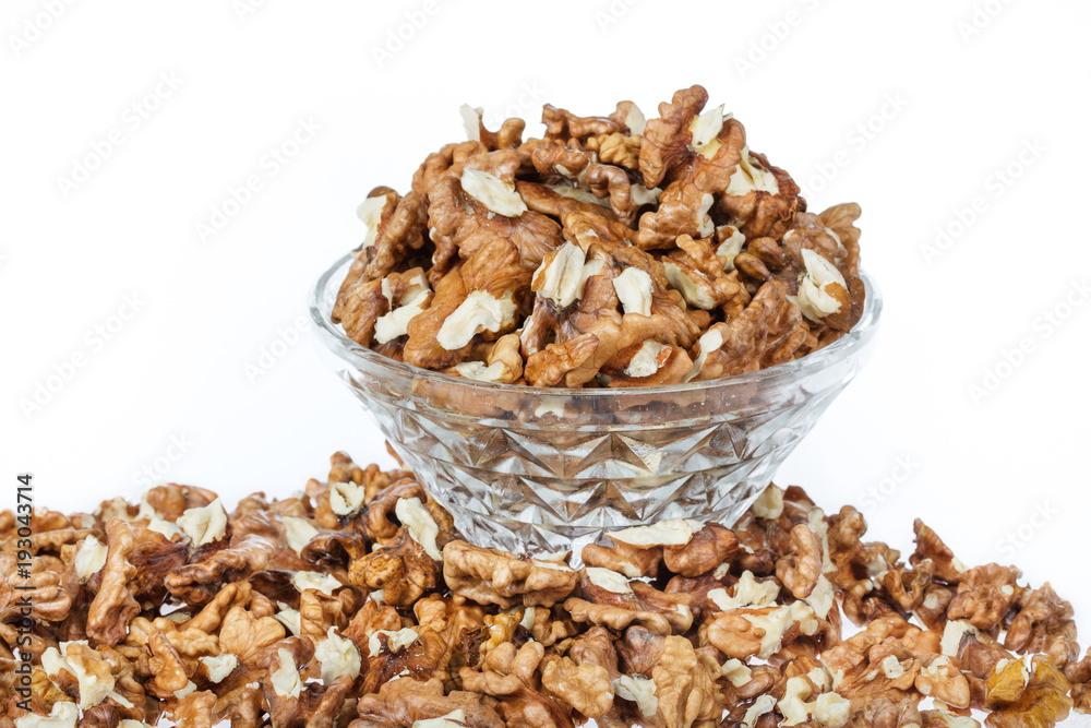 Cracked walnuts in glass bowl on white background