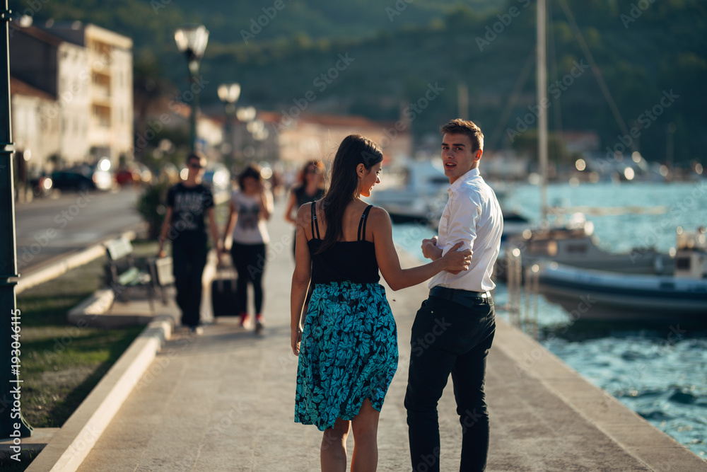 Young couple walking along the coastal lane in sunset.Man turning to see another woman,seeing ex girlfriend.Turning on and looking back over his shoulder.
