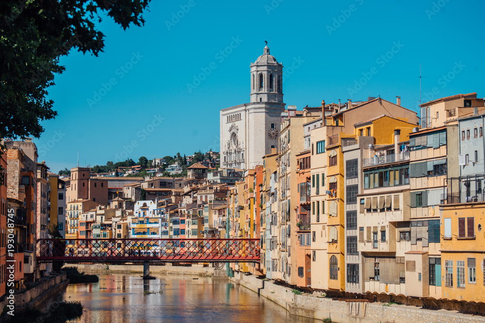 Colorful yellow and orange houses and bridge Pont de Sant Agusti reflected in water river Onyar, in Girona, Catalonia, Spain.