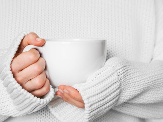 Warming cup of tea in the hands of woman in white sweater.