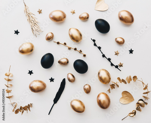 Flat lay composition with Easter eggs. Gold and black eggs over white background