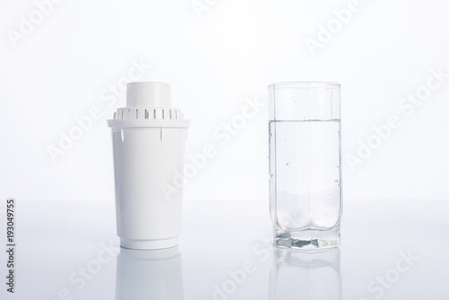 Replacement water filter and glass of purified water on white background, reflection