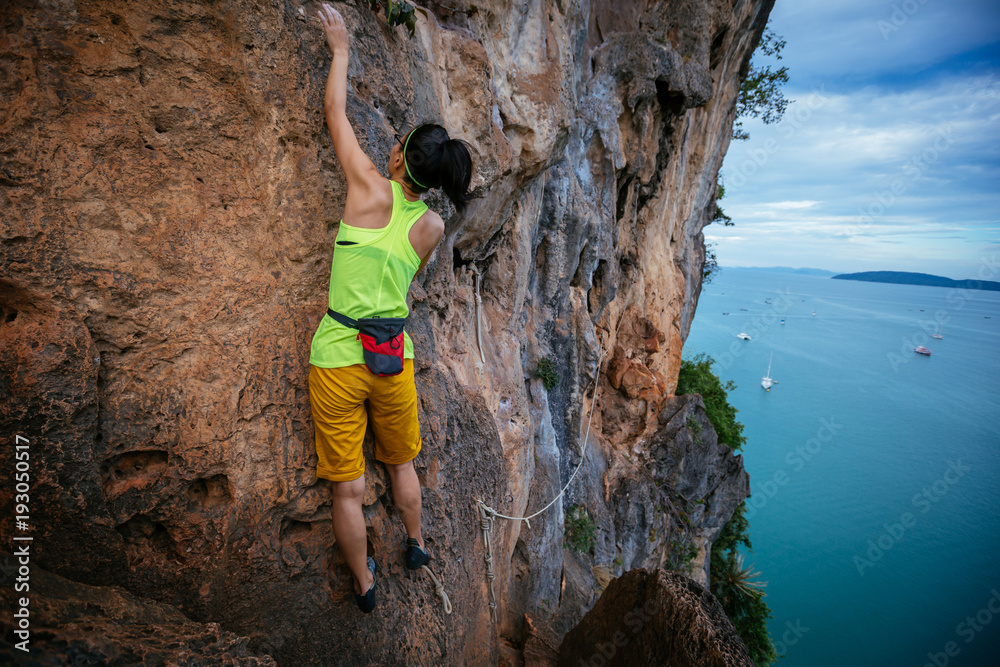 female rock climber climbing on seaside cliff