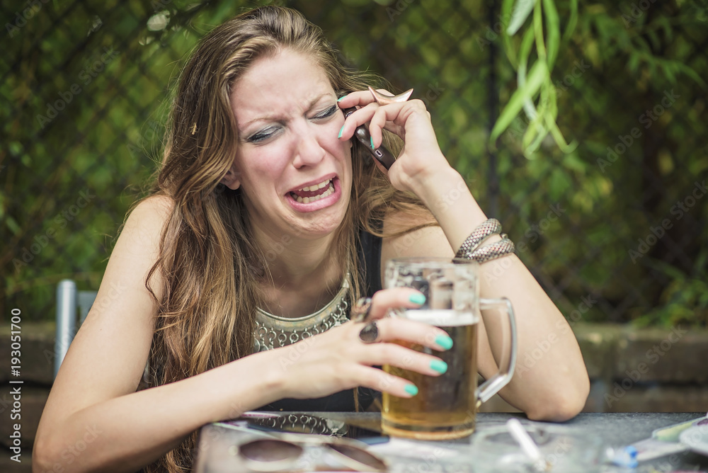 Heart broken girl crying over her cellphone, drunk, drinking a beer in a bar Stock Photo Adobe