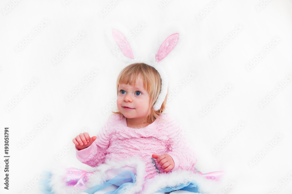 Fototapeta premium Closeup Portrait of Blonde Baby 18 month old Girl with Big Blue Eyes and Bunny Ears headband, Pink Tutu, isolated on white background.