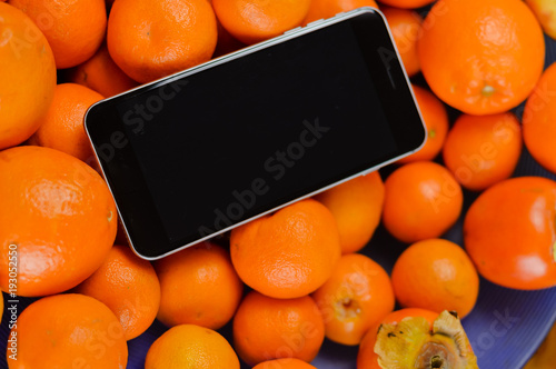 Closeup of mobile phone over fresh orange fruits background. Mockup flat lay digital communication technology design healthy natural diet photo