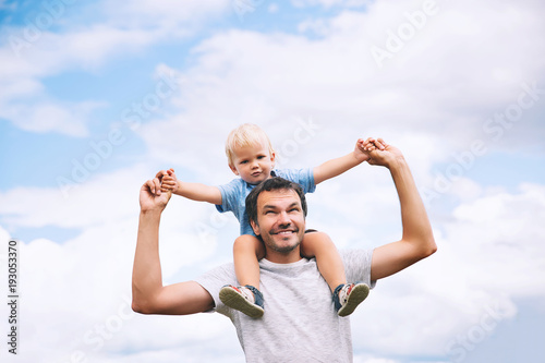 Father and son with raised arms up against the sky.