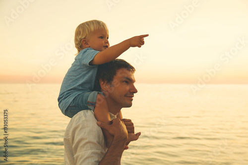 Canvas-taulu Father and son silhouettes at sunset on a sea beach.