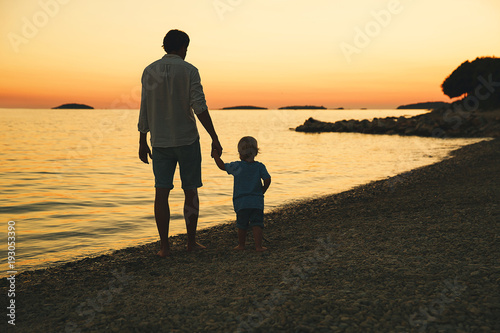 Father and son back silhouettes walking by the sea. photo