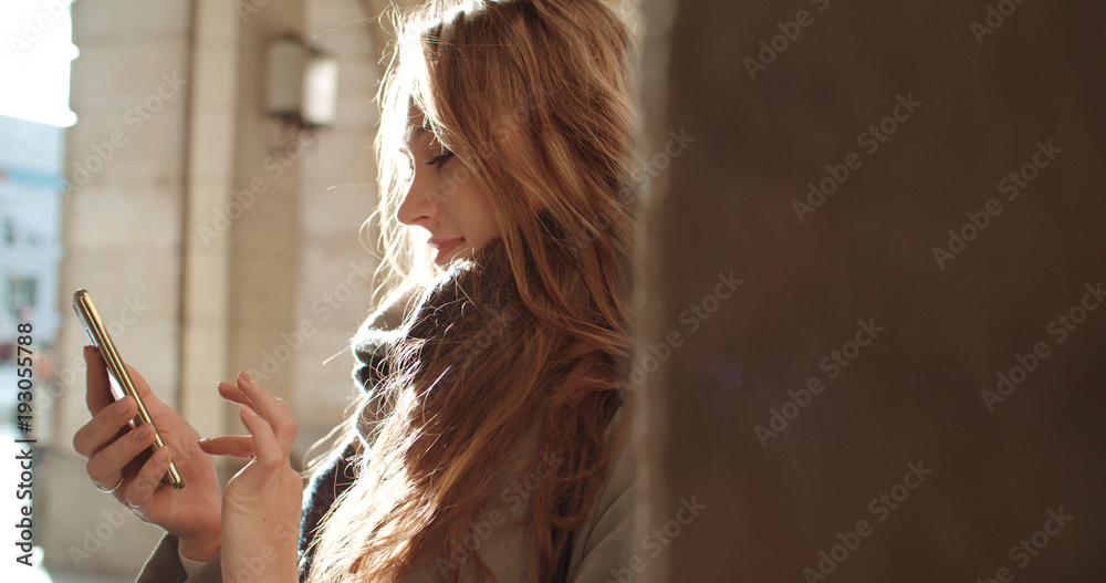 Fototapeta premium Beautiful young woman typing on phone during sunny day.