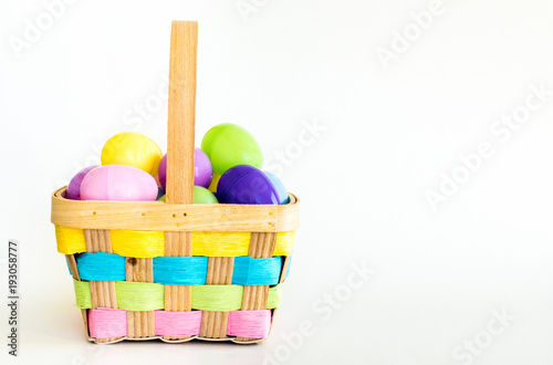 wicker Easter basket with colorful weaved ribbons filled with plastic Easter eggs isolated on white photo