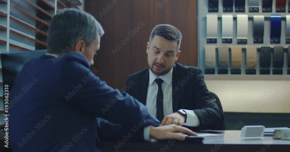 Elegant man paying with credit card then receiving car key in showroom