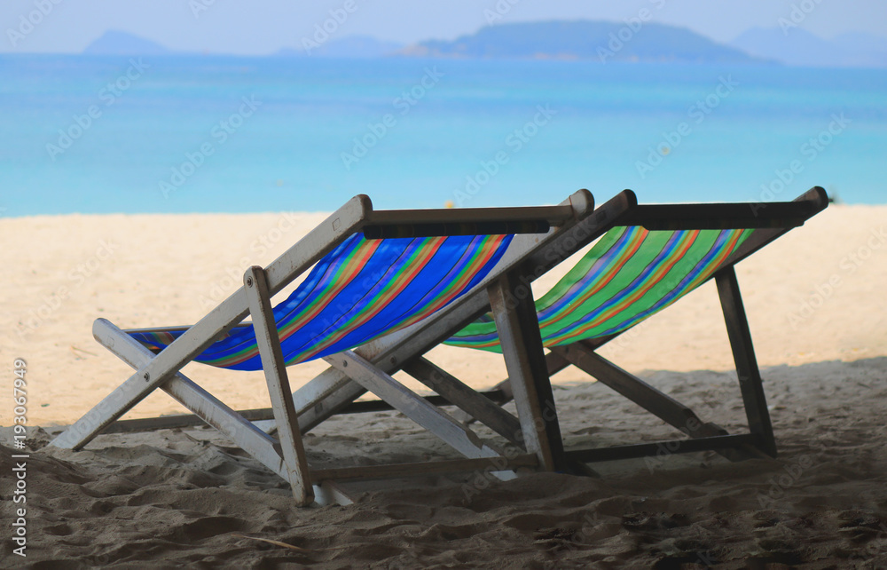 Beach chairs on the white sand beach with cloudy blue sky and sun