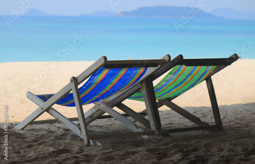 Beach chairs on the white sand beach with cloudy blue sky and sun © mansong