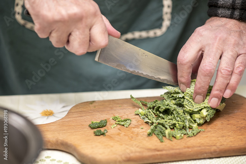 Elderly man, a domestic cook, cutting small pieces of green vegetable, borecole, to prepare for lunch