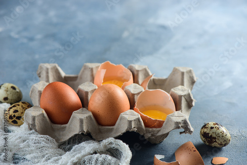 Fresh quail and chicken eggs, whole and broken, in a paper packaging on a concrete background. Raw ingredients for Easter cooking. Close-up with copy space photo