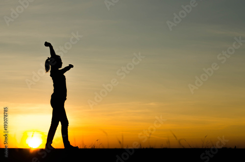 Woman silhouette is standing, raise one's hand for exercise, on evening .