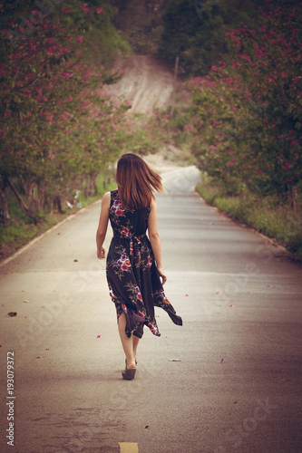Young woman in black dress with flower pattern background walking on a country road in the forest in summer season. Photo toned style Instagram filters