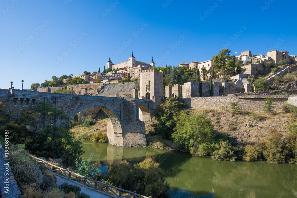 Shot from green water river Tagus, Tajo in Spanish, of Alcantara arch bridge and door,  landmark and monument from ancient Roman age, in Toledo city, Spain, Europe
