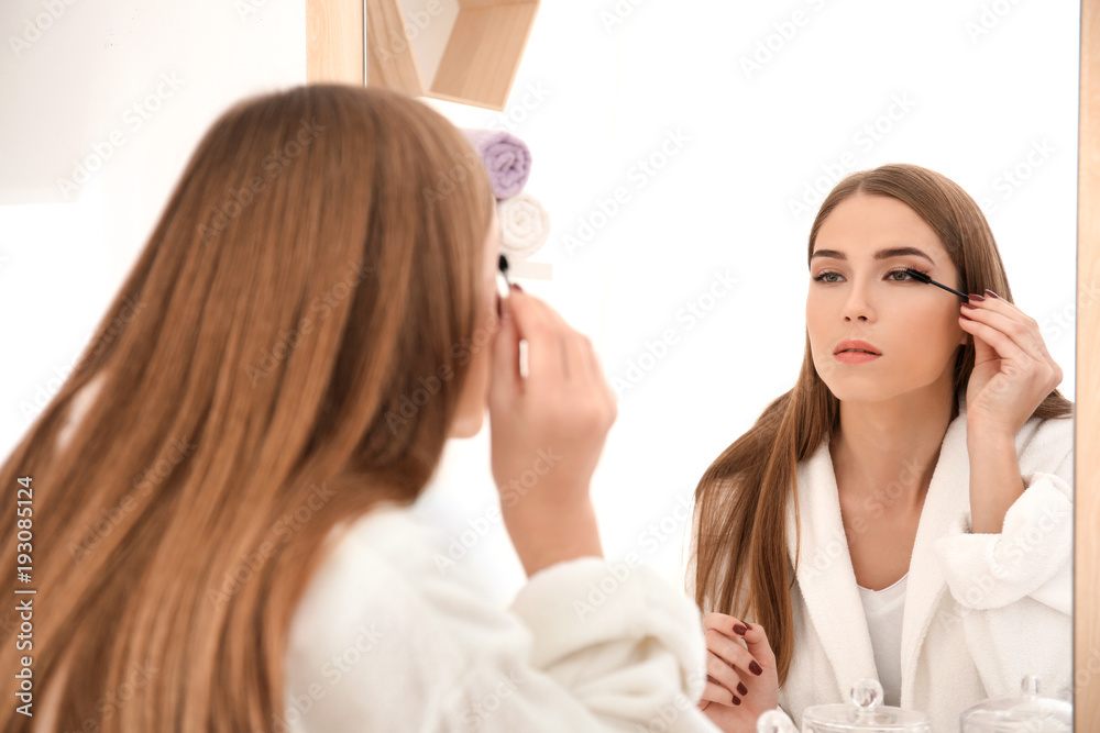 Young woman applying mascara on her eyelashes indoors Young woman applying mascara on her eyelashes indoors