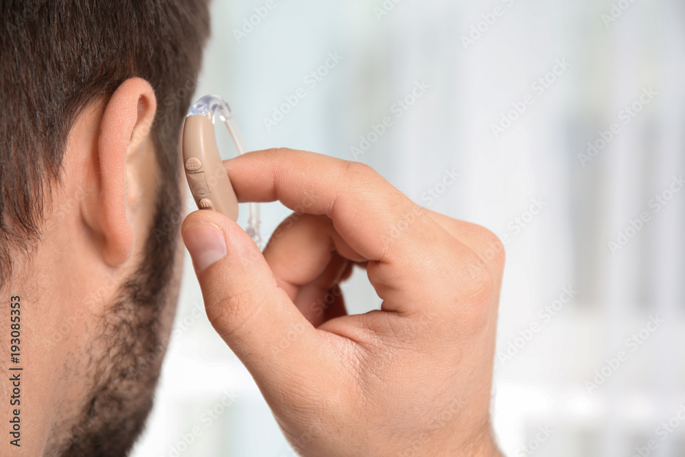 Fototapeta premium Young man putting hearing aid in ear indoors