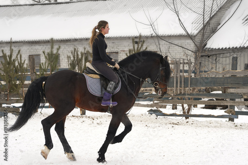 A girl on a horse jumps gallops. A girl trains riding a horse in a small paddock. A cloudy winter day.