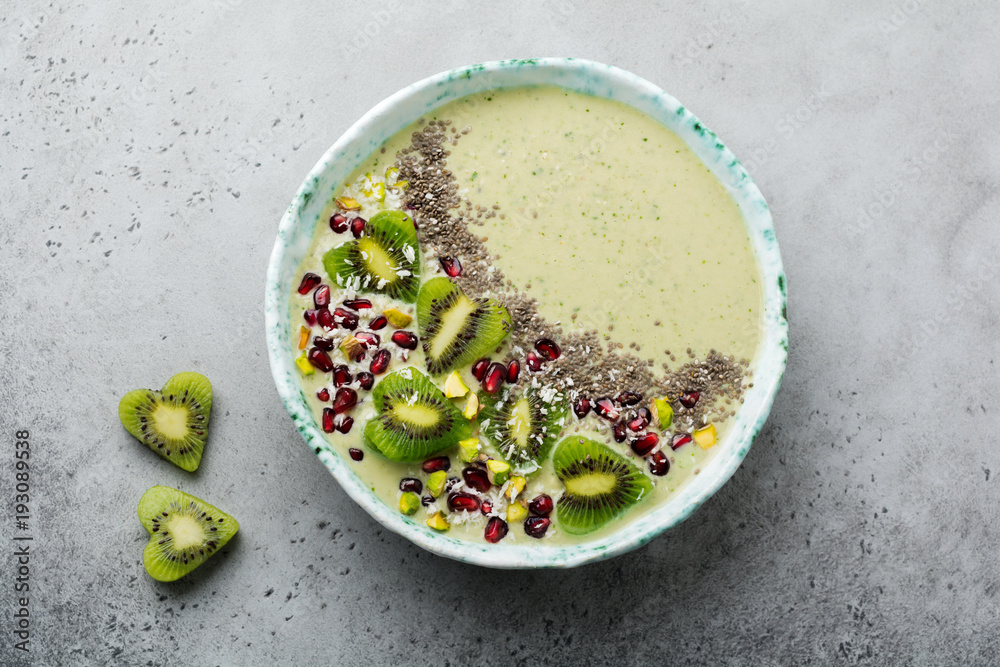 Kiwi banana smoothies bowl with oatmeal, pistachio nuts, pomegranate seeds and chia on light gray stone background. Selective focus. Top view. Copy space. Kiwi banana smoothies bowl with oatmeal, pistachio nuts, pomegranate seeds and chia on light gray stone background. Selective focus. Top view. Copy space.