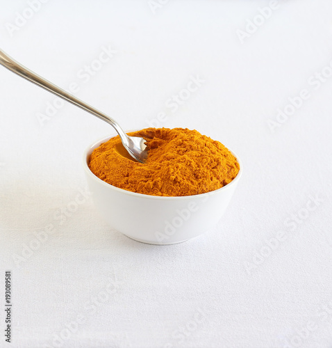 Turmeric powder, or haldi, traditional and popular ingredient used in many Indian dishes, scooped with a steel spoon from a white ceramic bowl.