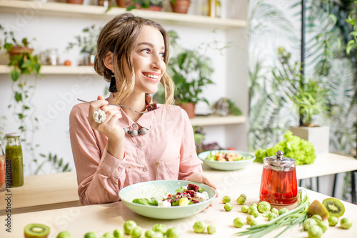 Young woman sitting with healthy food in the beautiful interior with green flowers on the background
