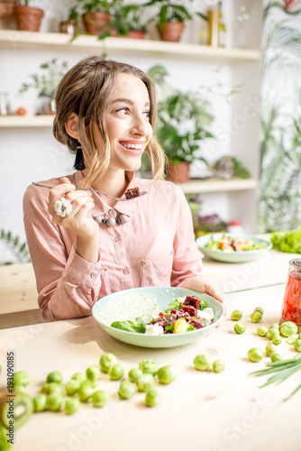 Young woman sitting with healthy food in the beautiful interior with green flowers on the background