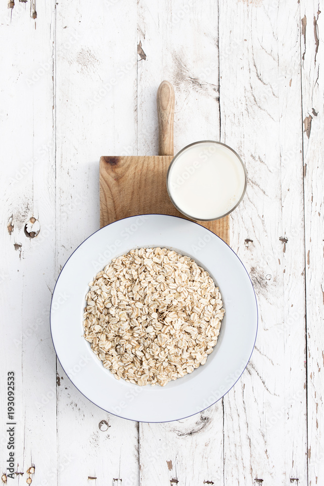 Oatmeal, rolled oats on white wooden background wilt glass of milk. Porridge oats, used in granola or muesli. Breakfast concept Oatmeal, rolled oats on white wooden background wilt glass of milk. Porridge oats, used in granola or muesli. Breakfast concept
