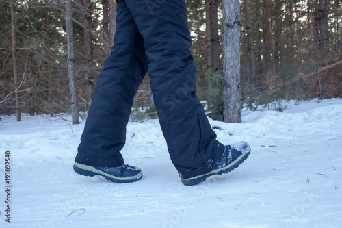 Woman legs in boots close up the snow-covered path in the winter forest, rear view