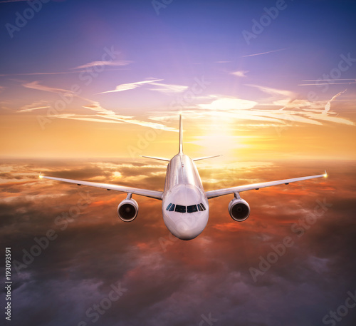 Airplane jetliner flying above clouds in beautiful sunset