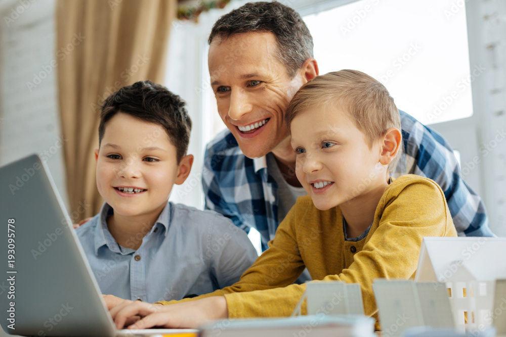 Nice job. Upbeat young father watching the presentation of their sons project on the laptop related to the alternative sources of energy and smiling, being proud of them Nice job. Upbeat young father watching the presentation of their sons project on the laptop related to the alternative sources of energy and smiling, being proud of them