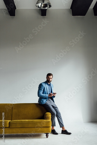 fashionable elegant man in blue suit using smartphone at yellow sofa