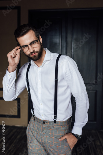 fashionable man posing in glasses, white shirt and suspenders
