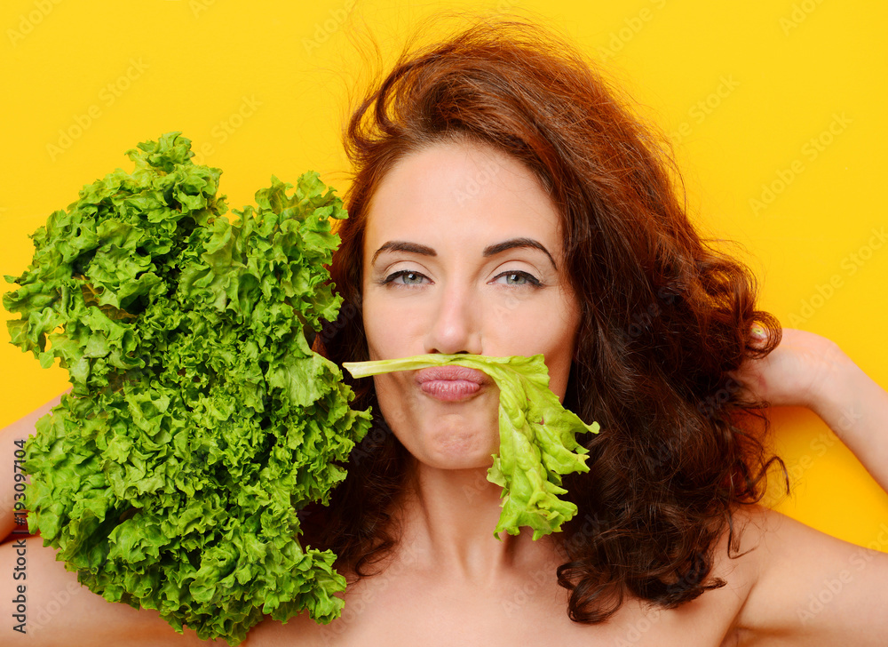 Pretty curly hair woman eat lettuce salad looking at the corner on yellow background Pretty curly hair woman eat lettuce salad looking at the corner on yellow background