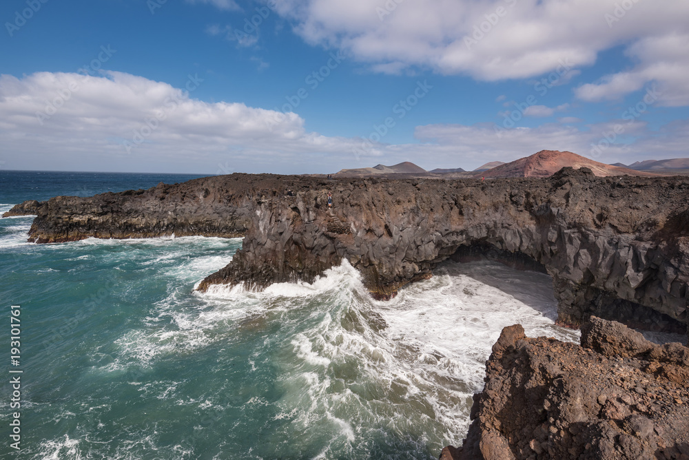 Lanzarote landscape. Los Hervideros coastline, lava caves, cliffs and wavy ocean. Unidentifiable tourist are in the background