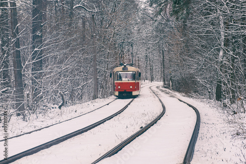 Red tram moving on the rails in the winter snowy forest, seasonal background