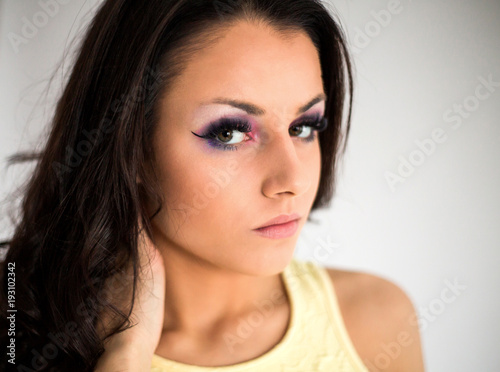 Portrait of attractive young brunette woman posing against light studio background close up