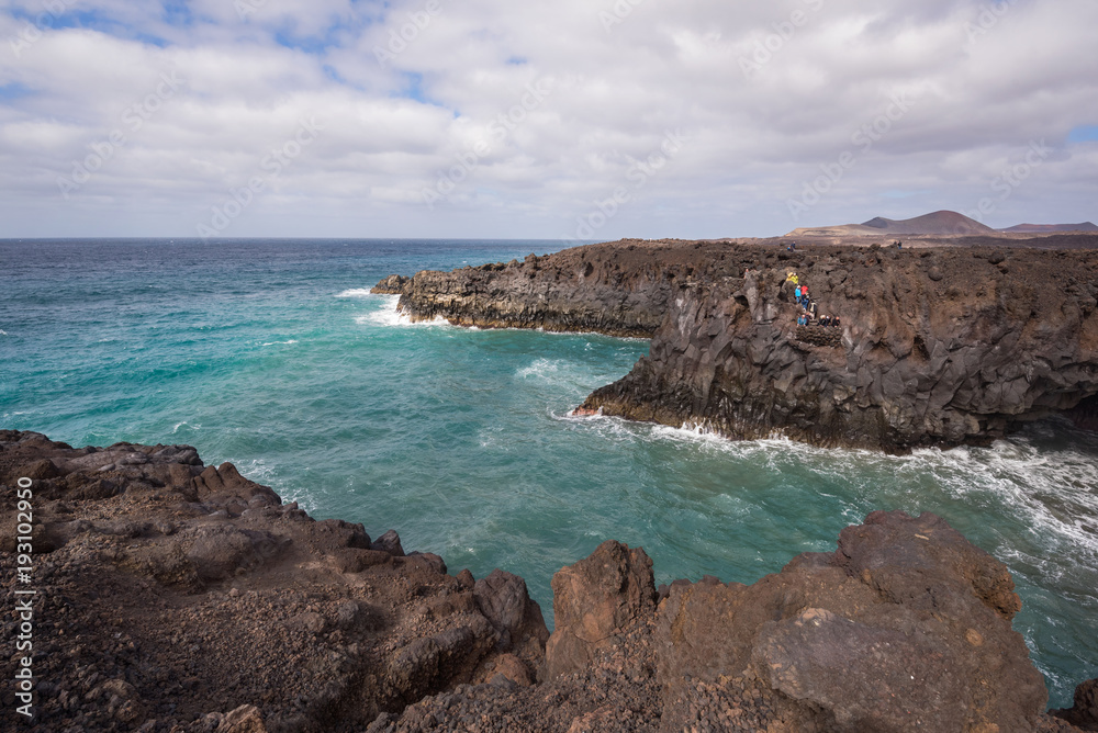 Lanzarote landscape. Los Hervideros coastline, lava caves, cliffs and wavy ocean. Unidentifiable tourist are in the background