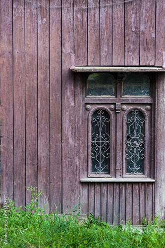 Old vintage window on a wooden house. brown background. Green grass at the bottom.