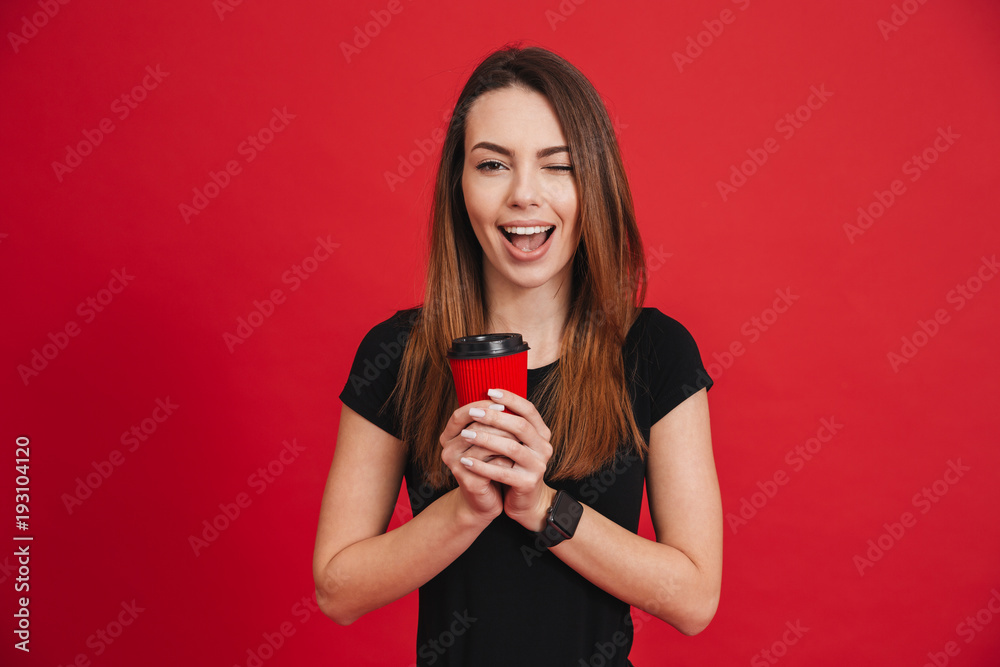 Image of positive woman with long brown hair playfully looking on camera and holding takeaway coffee in hands, isolated over red background Image of positive woman with long brown hair playfully looking on camera and holding takeaway coffee in hands, isolated over red background